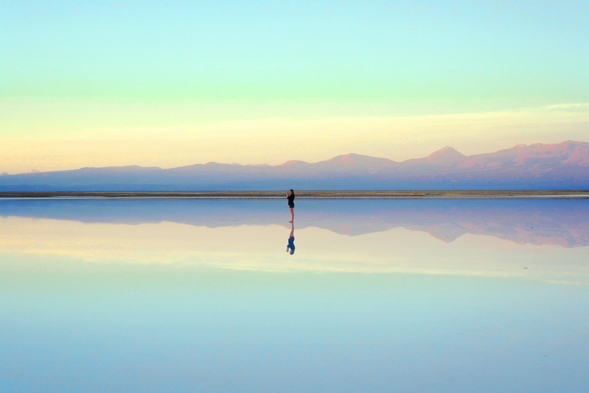 A person standing in shallow water reflecting the sky and horizon